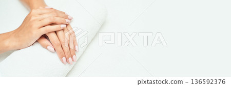 Close-up of female hands with light pink manicure resting on white towel 136592376