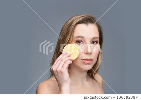 Young caucasian female with facial sponge for skincare routine on gray Young caucasian female with facial sponge for skincare routine on gray 136592387