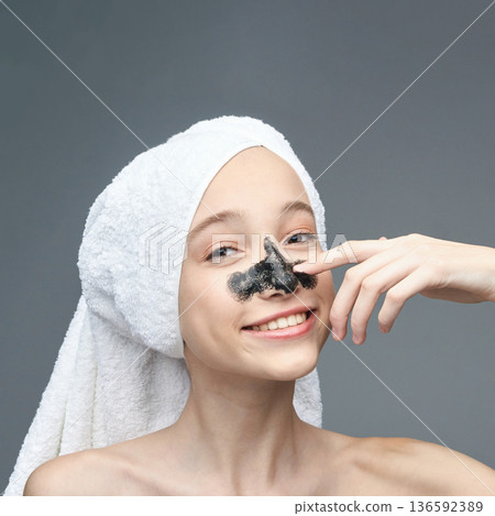 Young caucasian female applying charcoal face mask with towel on head smiling Young caucasian female applying charcoal face mask with towel on head smiling 136592389