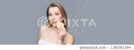 Young caucasian female using facial sponge for skincare routine on gray Young caucasian female using facial sponge for skincare routine on gray 136592394
