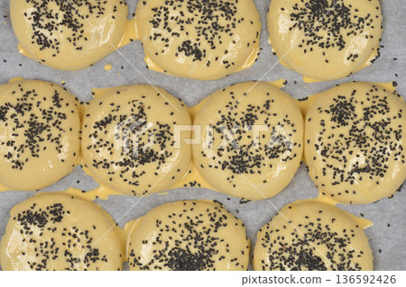 Raw buns with black sesame seeds on baking paper Raw buns with black sesame seeds on baking paper 136592426