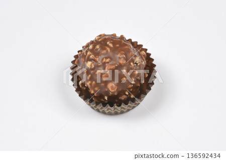 Chocolate truffle with hazelnuts in a paper liner on a white background 136592434