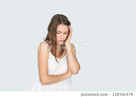 Young caucasian female appearing stressed or unwell with hand on head in white Young caucasian female appearing stressed or unwell with hand on head in white 136592479