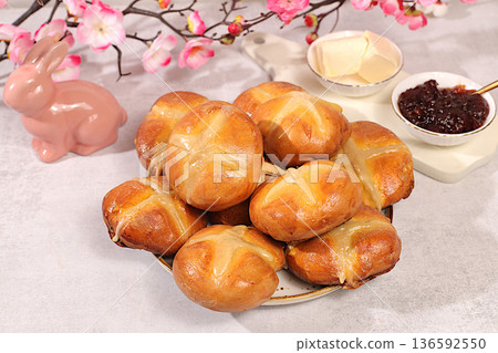 Festive Easter treat. Easter buns with a cross, jam, butter, and cherry blossoms. English buns are baked on Friday and served with tea the morning before Easter Sunday. Happy Easter concept. 136592550