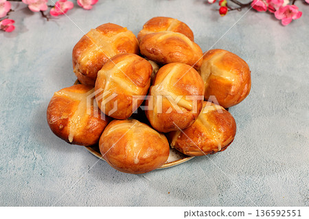 Happy Easter concept. Easter buns with a cross on a concrete table and cherry blossoms. English buns are baked on Friday and served with tea the morning before Easter Sunday. A festive Easter treat 136592551
