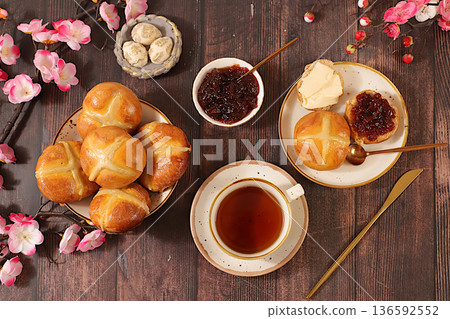 Happy Easter concept . Easter buns with a cross and jam, butter, and cherry blossoms. English buns are baked on Friday and served with tea the morning before Easter Sunday. A festive Easter treat Happy Easter concept . Easter buns with a cross and jam, butter, and cherry blossoms. English buns are baked on Friday and served with tea the morning before Easter Sunday. A festive Easter treat 136592552