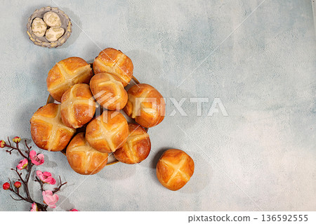 Happy Easter concept. Easter buns with a cross on a concrete table and cherry blossoms. English buns are baked on Friday and served with tea the morning before Easter Sunday. A festive Easter treat 136592555