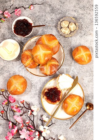 Happy Easter concept . Easter buns with a cross and jam, butter, and cherry blossoms. English buns are baked on Friday and served with tea the morning before Easter Sunday. A festive Easter treat 136592559
