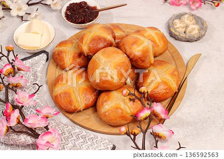 Festive Easter food concept. Easter buns are topped with cross, jam, butter, and cherry blossom branches. English buns are baked on Good Friday and served with tea on the morning before Easter Sunday 136592563