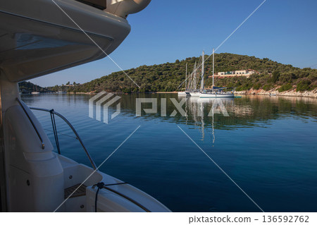 Moored sailboats on the coast of Atherinos Bay, Meganisi island, Ionian Sea, Greece in the summer morning. Horizontal. Moored sailboats on the coast of Atherinos Bay, Meganisi island, Ionian Sea, Greece in the summer morning. Horizontal. 136592762