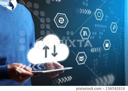 Hands holding tablet with cloud icons showing data transfer in a tech workspace during day 136592810