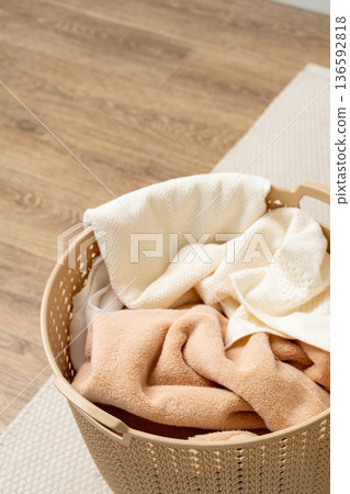 Laundry basket holds clean towels in a room with wooden floor and light decor Laundry basket holds clean towels in a room with wooden floor and light decor 136592818