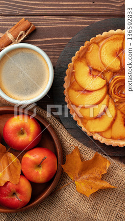 Sliced peach tart with apples, cinnamon sticks, and coffee on a wooden table at fall time Sliced peach tart with apples, cinnamon sticks, and coffee on a wooden table at fall time 136592833
