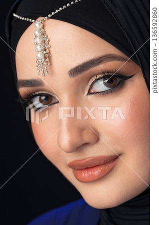 Woman wearing hijab with jewelry on forehead and subtle makeup in close-up view Woman wearing hijab with jewelry on forehead and subtle makeup in close-up view 136592860