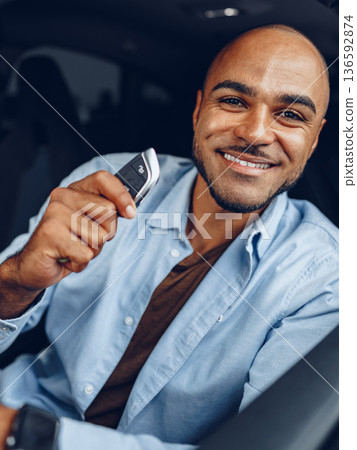 Man smiles while holding car key inside a vehicle on a sunny day in the city 136592874