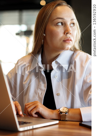 Woman using laptop in a cafe during the day while looking out towards the side Woman using laptop in a cafe during the day while looking out towards the side 136592910