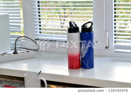 Two thermoses are standing on the windowsill. Two thermoses are standing on the windowsill. 136592976