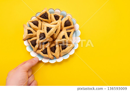 Hands holding Hamantaschen cookie isolate on yellow background. 136593009