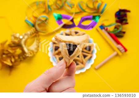 Hands holding Hamantaschen cookie isolate on yellow background. 136593010