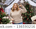 Young woman in sweater decorating Christmas tree at home and smiling. Winter time and holidays. Celebration banner 136593216