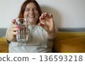 Dietary supplement, healthy diet positive young woman hand holding pill capsule, take vitamin in mouth for beauty skin hair, taking medicine with glass of water at home, pharmacy and health care 136593218