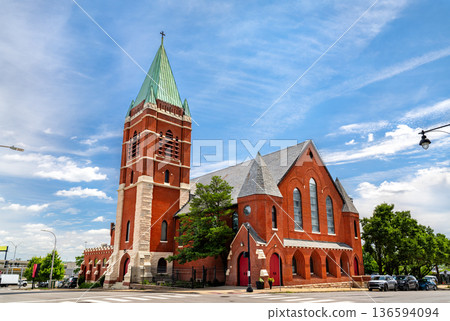 St. Mary's Episcopal Church in Kansas City Missouri. Historic Gothic Revival architecture features a red brick facade with a green copper spire and arched windows under a blue sky St. Mary's Episcopal Church in Kansas City Missouri. Historic Gothic Revival architecture features a red brick facade with a green copper spire and arched windows under a blue sky 136594094