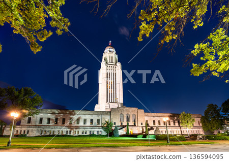 Nebraska State Capitol in Lincoln at night. Historic Art Deco skyscraper features a limestone tower and gold dome illuminated against a dark blue sky Nebraska State Capitol in Lincoln at night. Historic Art Deco skyscraper features a limestone tower and gold dome illuminated against a dark blue sky 136594095