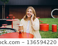 Happy 30s Woman Phone Call Cafe - Smiling woman talking on her phone while sitting at a table outside a cafe. 136594220