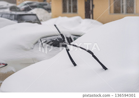 Snow covered car parked outdoors, heavy winter snowfall, windshield wipers raised above deep snow, winter car, snow car, frozen vehicle, parking after storm. Winter weather and transportation problems 136594301