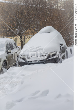 Car completely covered in deep snow during winter snowfall in residential area. Concept of cold weather, vehicle abandonment and seasonal parking difficulties 136594303