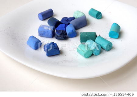 Blue and turquoise soft pastel crayons on a white plate. Art supplies for painting 136594409