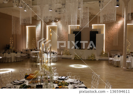 Elegant wedding banquet hall with decorated tables, candles and chandeliers in classic interior 136594611
