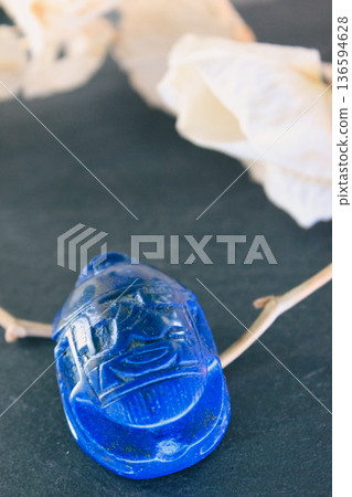 Lapis lazuli scarab beetle on dark slate surrounded by white petals and dry branches, sacred symbol. Lapis lazuli scarab beetle on dark slate surrounded by white petals and dry branches, sacred symbol. 136594628