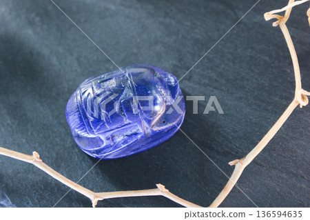 Lapis lazuli scarab beetle carving on dark slate stone with decorative dry branches, ancient amulet. 136594635