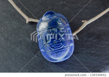 Lapis lazuli scarab beetle carving on dark slate stone with decorative dry branches, ancient amulet. 136594642