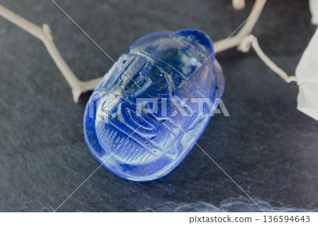 Lapis lazuli scarab beetle carving on dark slate stone with decorative dry branches, ancient amulet. 136594643