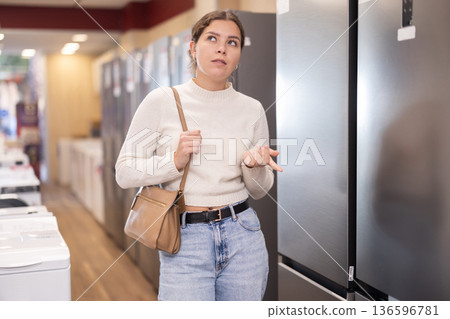Young woman buyer examine fridge in detail before buying Young woman buyer examine fridge in detail before buying 136596781