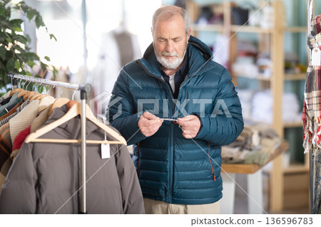 Elderly man trying on a down jacket Elderly man trying on a down jacket 136596783