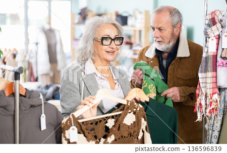 Mature married couple chooses fashionable warm dress and sweater in clothing store Mature married couple chooses fashionable warm dress and sweater in clothing store 136596839
