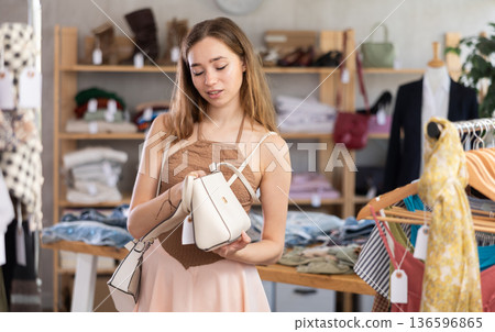 Happy young woman choosing handbag in clothing store Happy young woman choosing handbag in clothing store 136596865