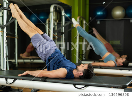 Young man doing pelvic lift exercise on reformer machine 136596898