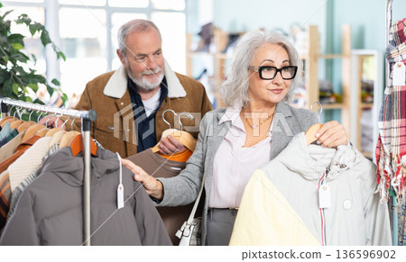 Mature couple spend time in shop and choose down jacket and T-shirt 136596902