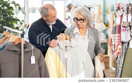Elderly couple chooses fashionable coat or jacket in clothing store Elderly couple chooses fashionable coat or jacket in clothing store 136596907