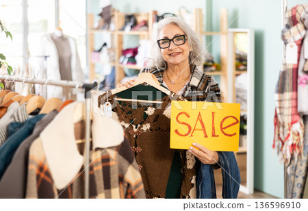 Mature woman holding a poster in her hands about a sale in a store Mature woman holding a poster in her hands about a sale in a store 136596910