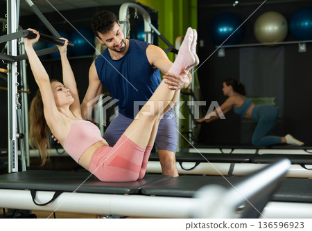 Male trainer guiding young girl doing leg presses on pilates chair 136596923