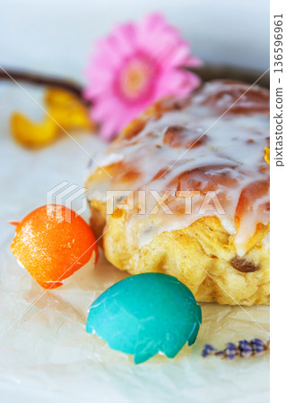 Closeup still life of glazed easter bread with gerbera daisy and cracked colorful easter egg shells on parchment paper. Soft focus Closeup still life of glazed easter bread with gerbera daisy and cracked colorful easter egg shells on parchment paper. Soft focus 136596961