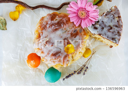 Overhead still life of glazed easter bread with gerbera daisy and cracked colorful easter egg shells on parchment paper. Soft focus Overhead still life of glazed easter bread with gerbera daisy and cracked colorful easter egg shells on parchment paper. Soft focus 136596963