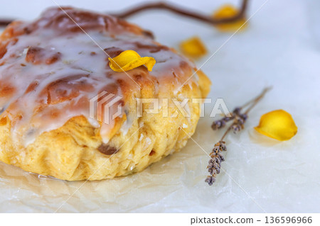 Still life of glazed easter bread on crinkled parchment with lavender sprigs and yellow petals on a white surface. Selective focus 136596966
