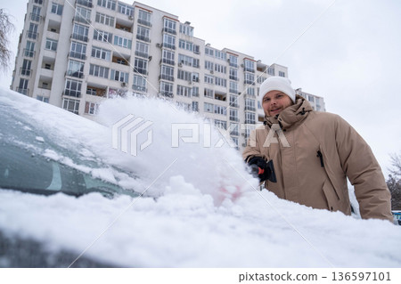 Man Clearing Snow from Car in Winter Cityscape Man Clearing Snow from Car in Winter Cityscape 136597101