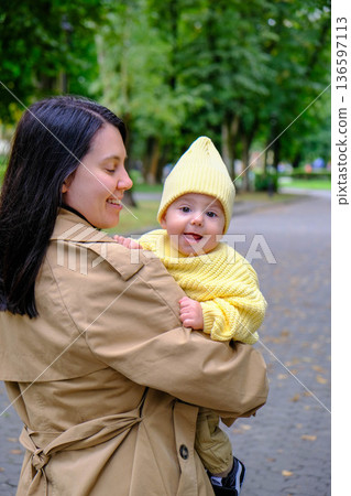 Mother Holding Baby in Yellow Outfit at Park Mother Holding Baby in Yellow Outfit at Park 136597113
